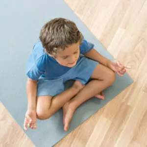 Boy sitting on yoga mat participating in The Play Projects OT At Home Yoga Program